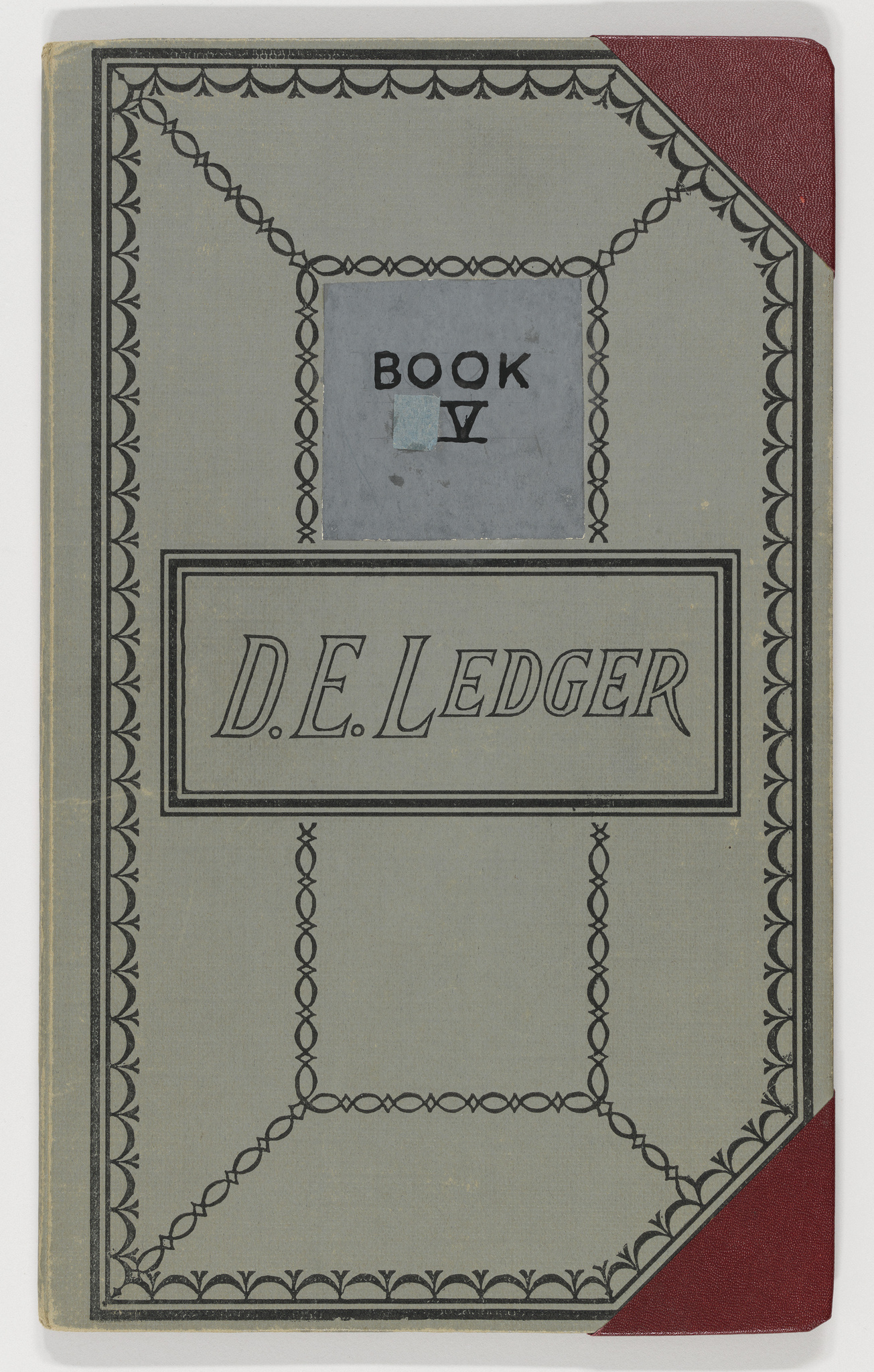 Vintage ledger book cover with "D.E. Ledger" text, decorative border, and red corner accent.